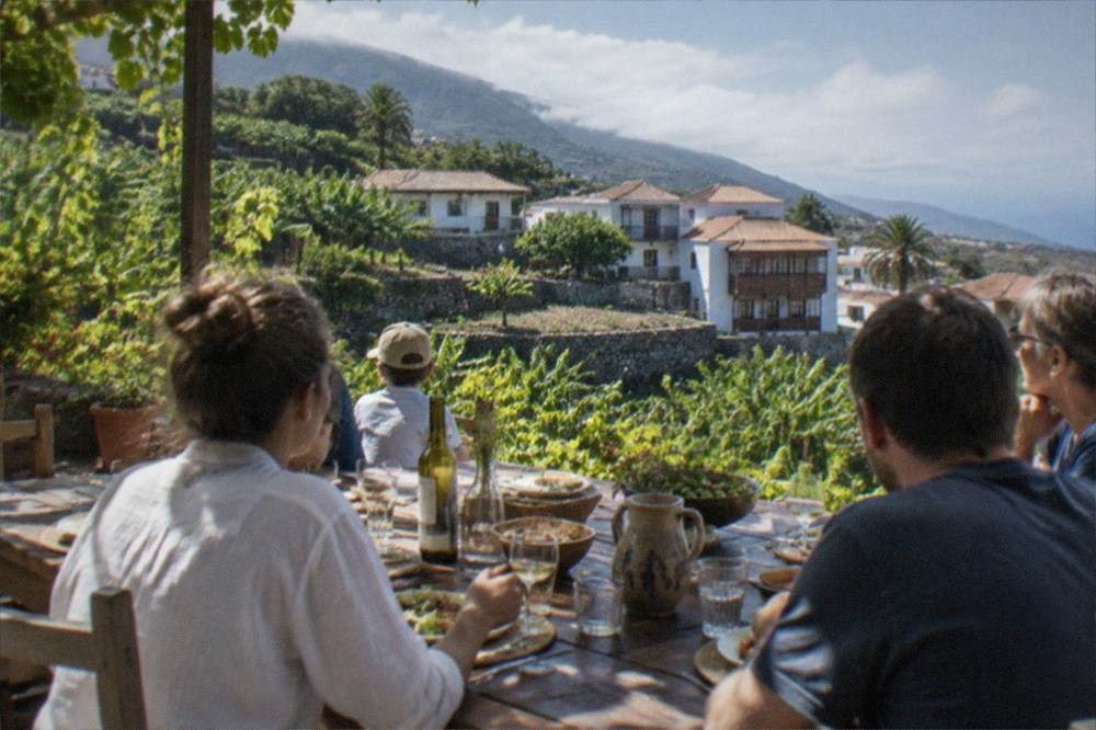 A family sharing a long lunch table at an outdoor terrace surrounded by vines