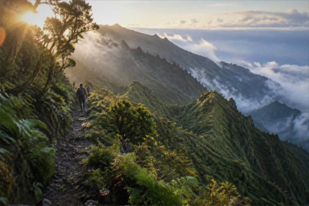 A ridge trail in the Anaga rural park with green slopes dropping toward the sea and low cloud offshore