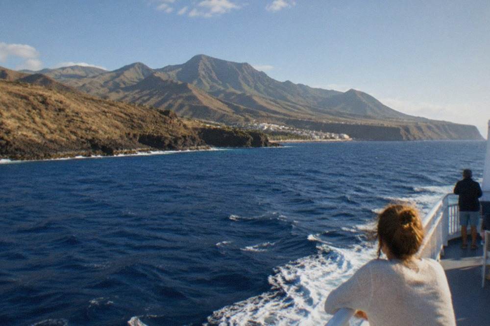 A ferry at sea with green Canary Island hills in the distance under a bright sky