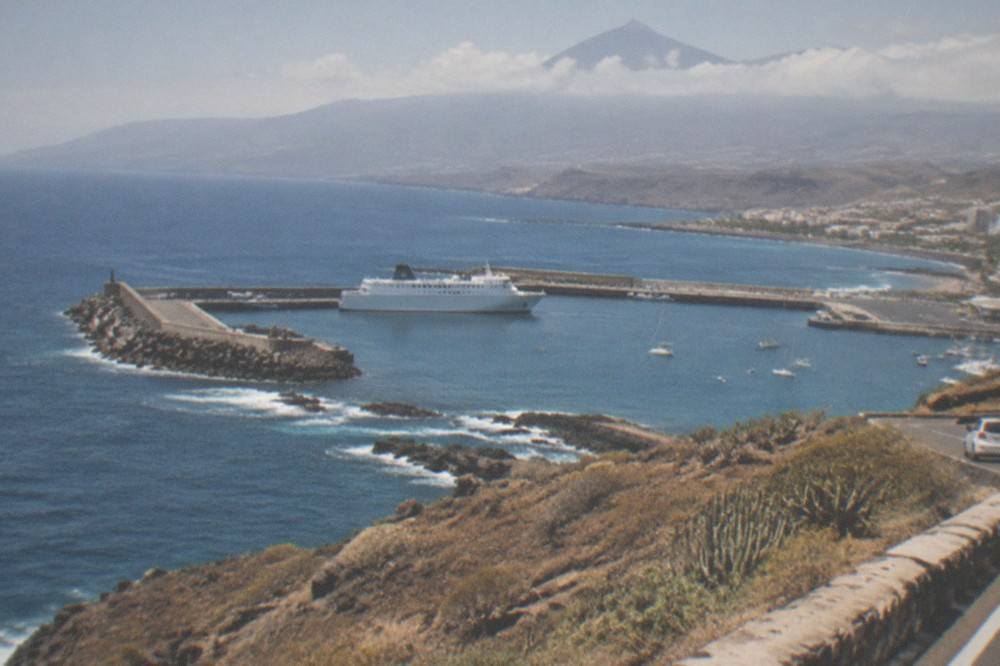 A volcanic mountain rising above clouds seen from a coastal road on Tenerife