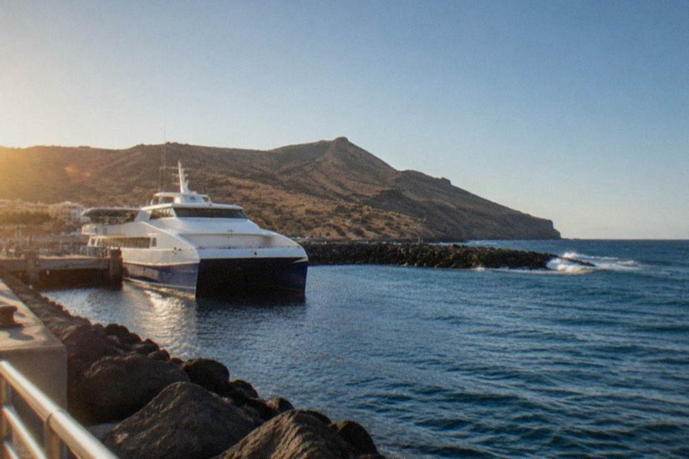 A catamaran ferry moored in a small Canary Island harbour with hills behind
