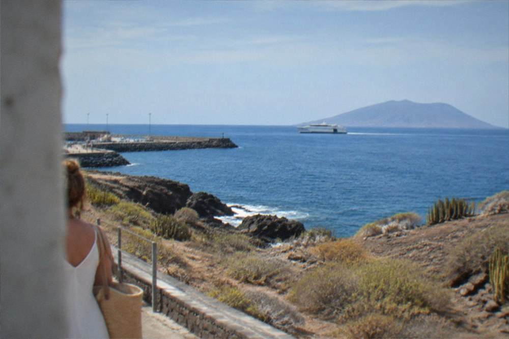 A calm blue sea with a distant ferry and a small island on the horizon in bright sunlight