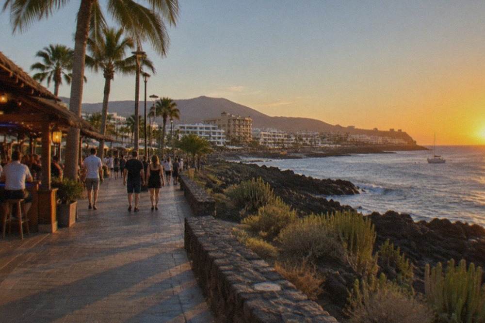 A lively seaside promenade at dusk with palm trees and lit bars along the waterfront