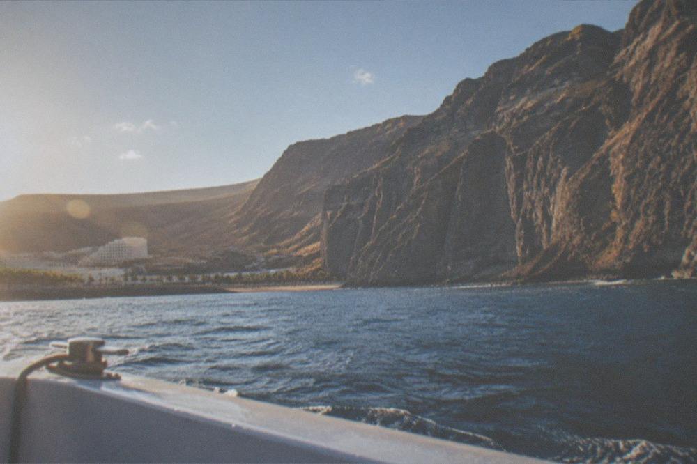 A boat approaching tall sea cliffs that rise sheer from blue water