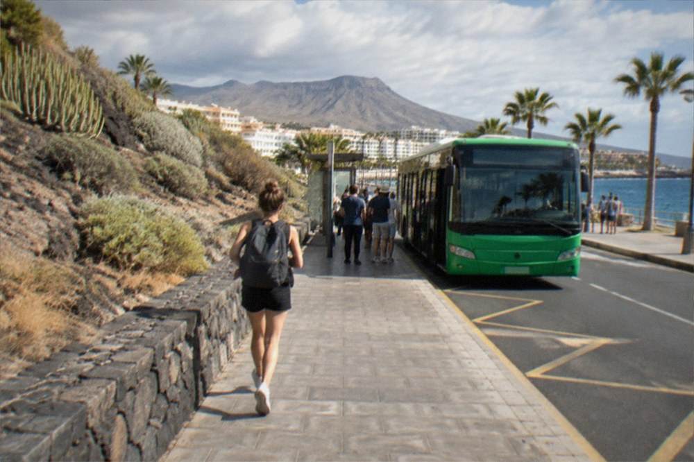 A green bus parked at a seaside stop with passengers waiting
