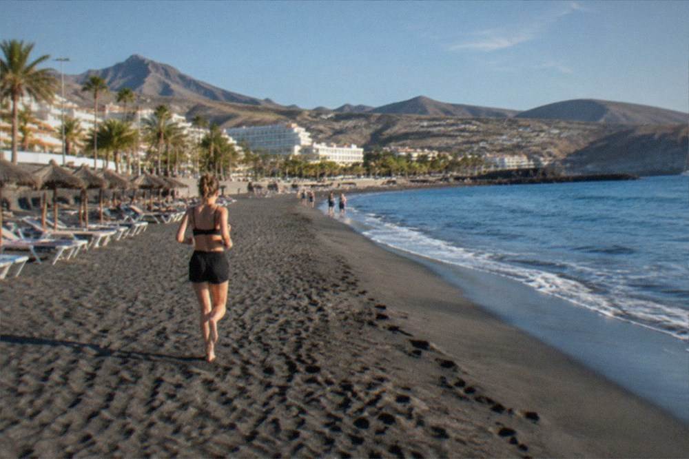 A wide sandy beach in bright sunshine with sun loungers and calm blue water