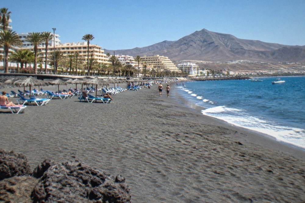 A wide sandy beach with sun loungers, parasols and resort buildings behind it