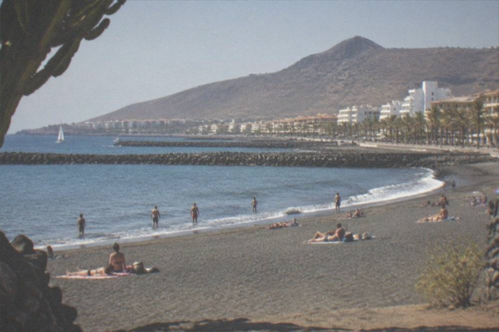 Sunbathers on a dark volcanic sand beach with breakwaters in the background