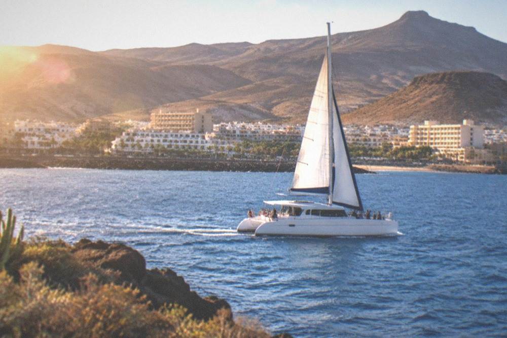 A catamaran with passengers sailing over open blue water near the Tenerife coast
