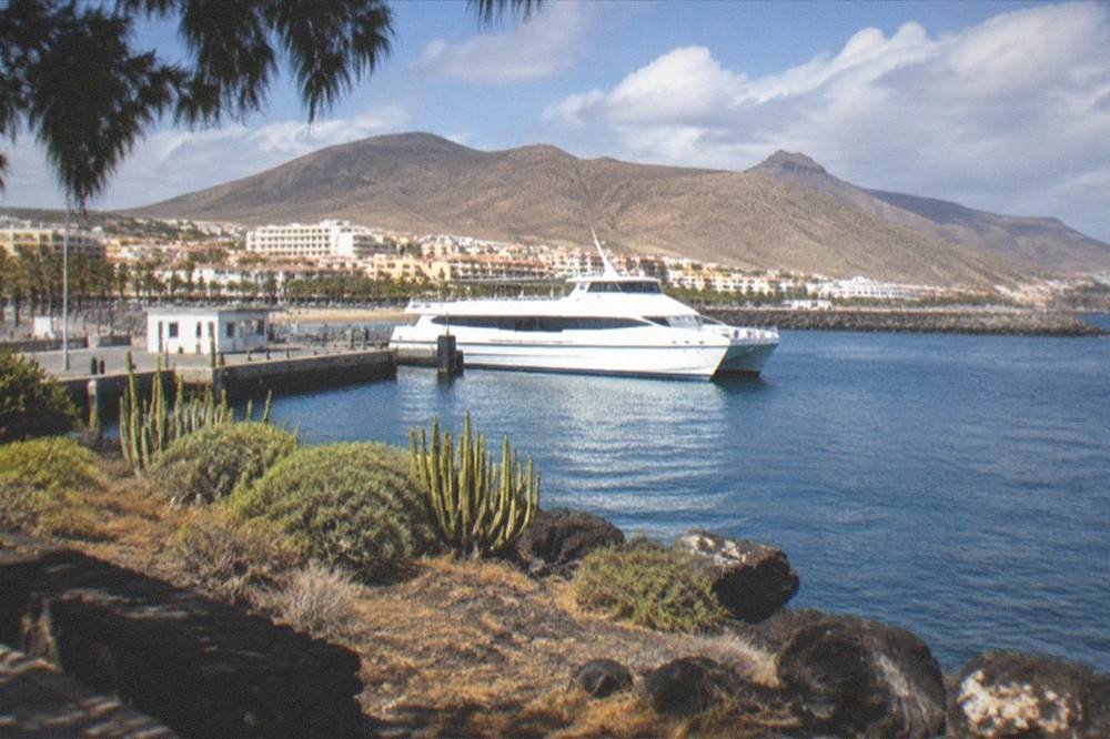 A white passenger ferry moored in a harbour with a town of low buildings behind it