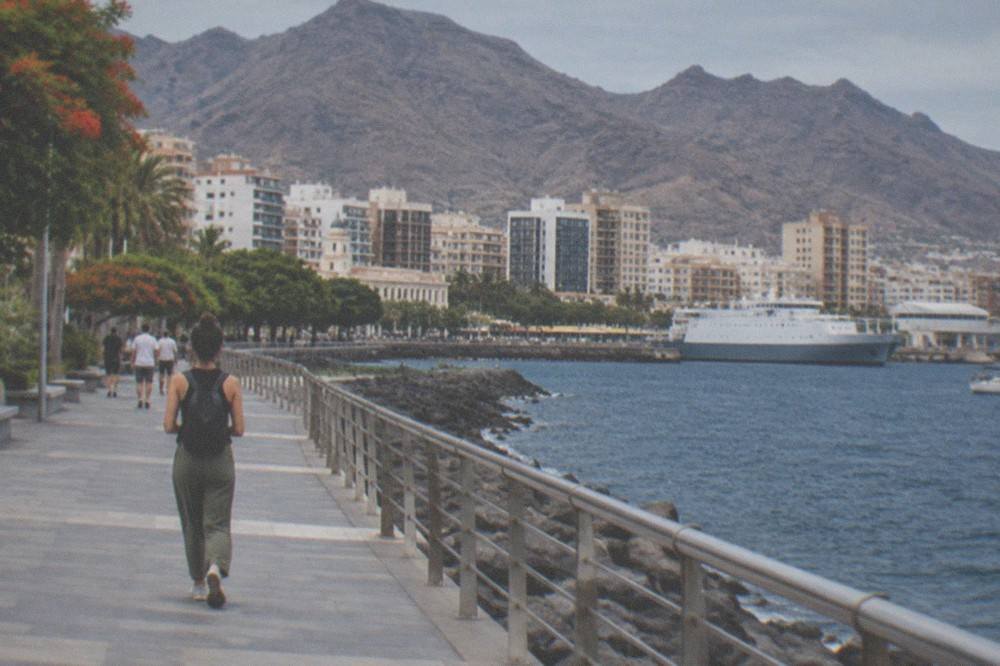 A traveller walking away along a seaside promenade with a small backpack