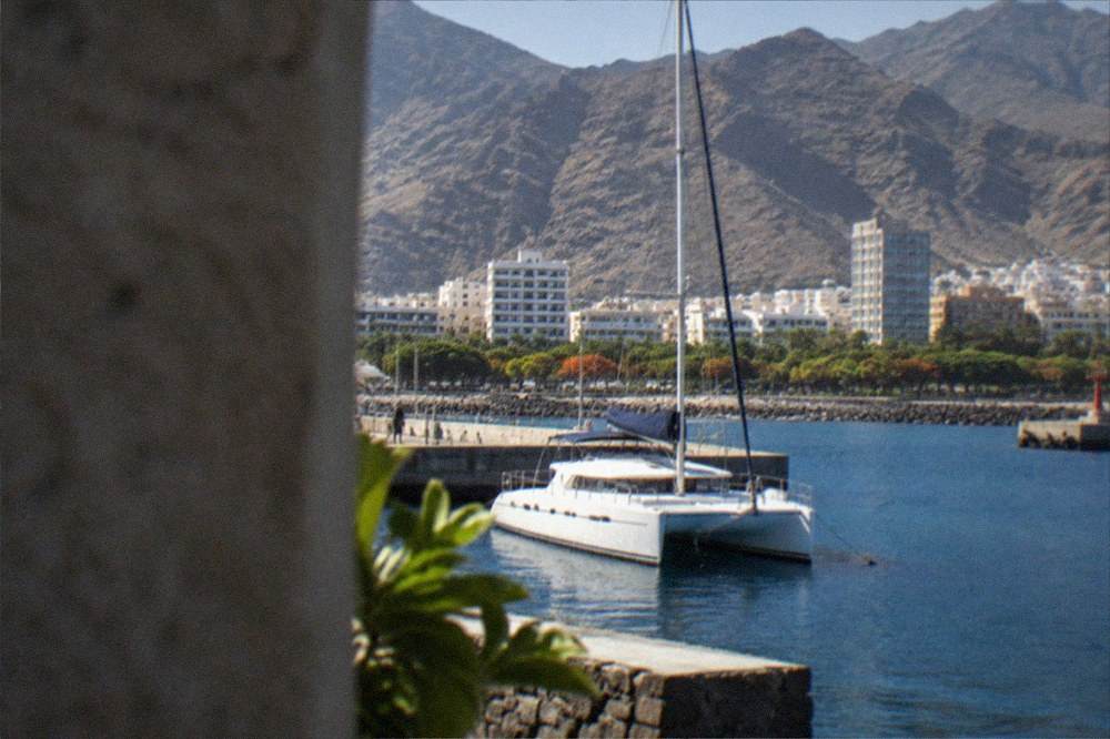 A catamaran moored in a small harbour below tall dark cliffs