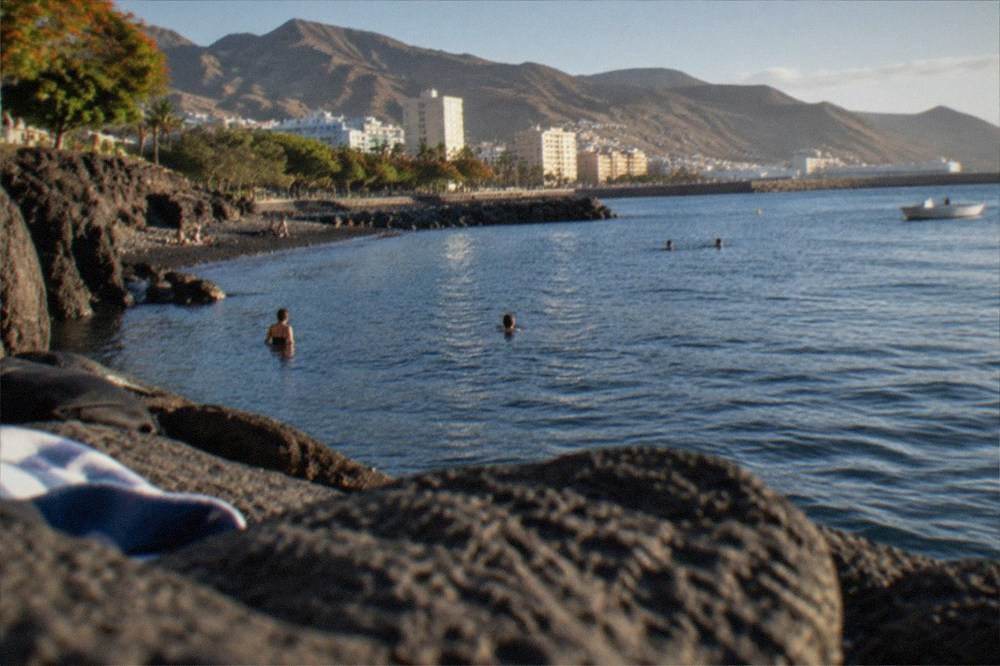 People swimming from a small cove beside calm blue water