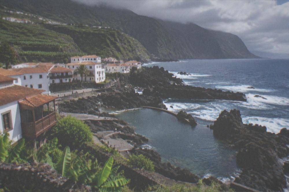 A small bay with clear water and volcanic rock at the foot of high cliffs