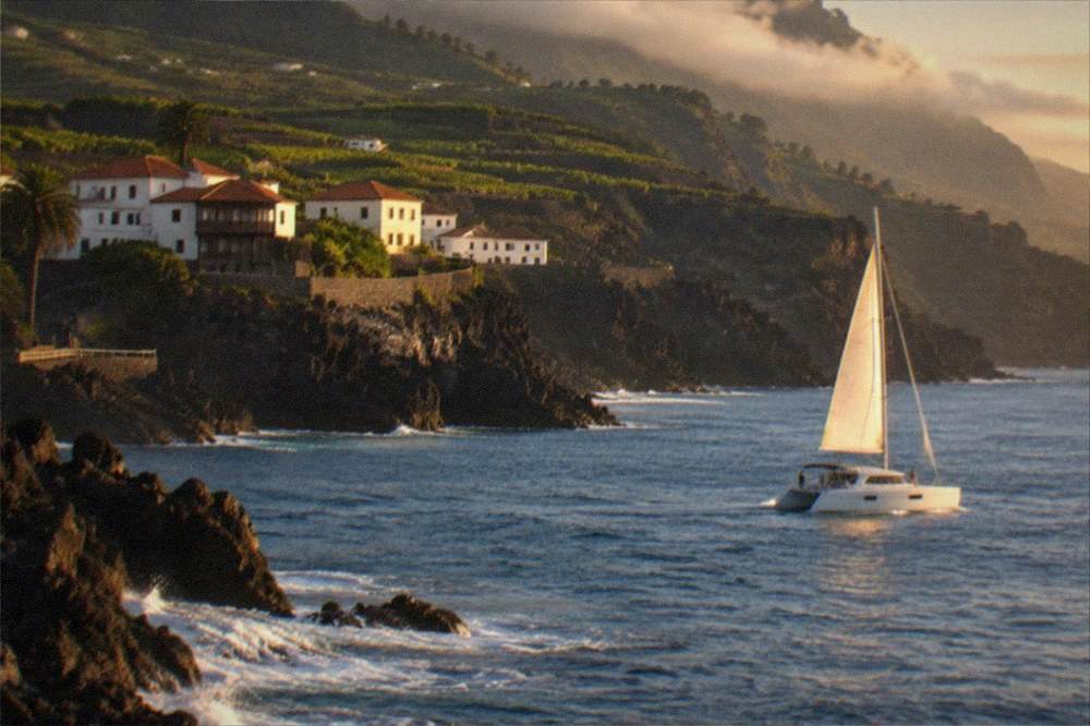 A catamaran near high dark cliffs above calm sea water
