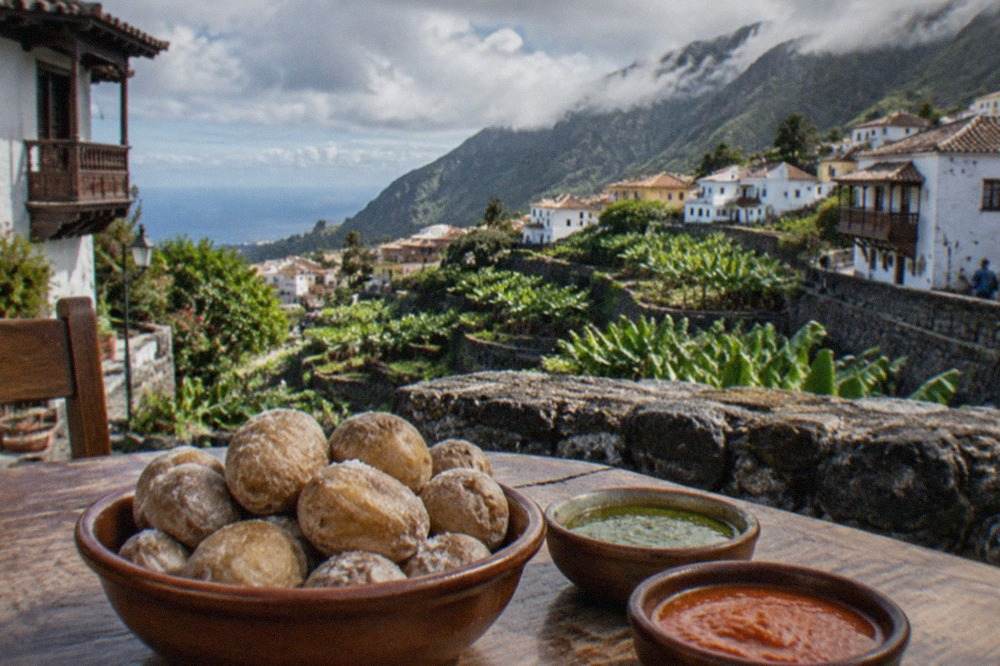 Small wrinkled potatoes with a salt crust in a bowl beside two dishes of red and green sauce