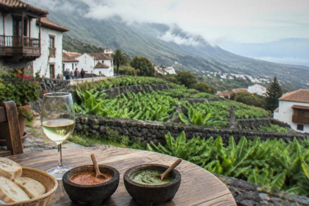Two stone bowls of red and green sauce on a table with bread and a glass of wine
