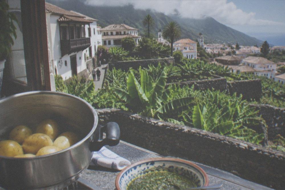 A pot of potatoes draining in a kitchen with a dish of sauce beside it