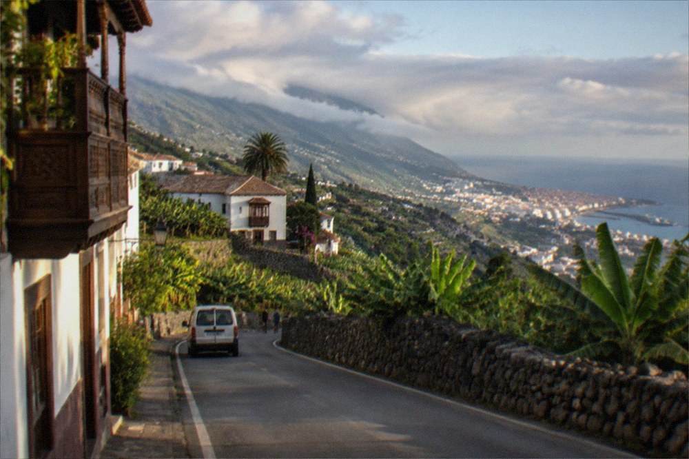 A coastal road above the sea with a town and harbour in the distance