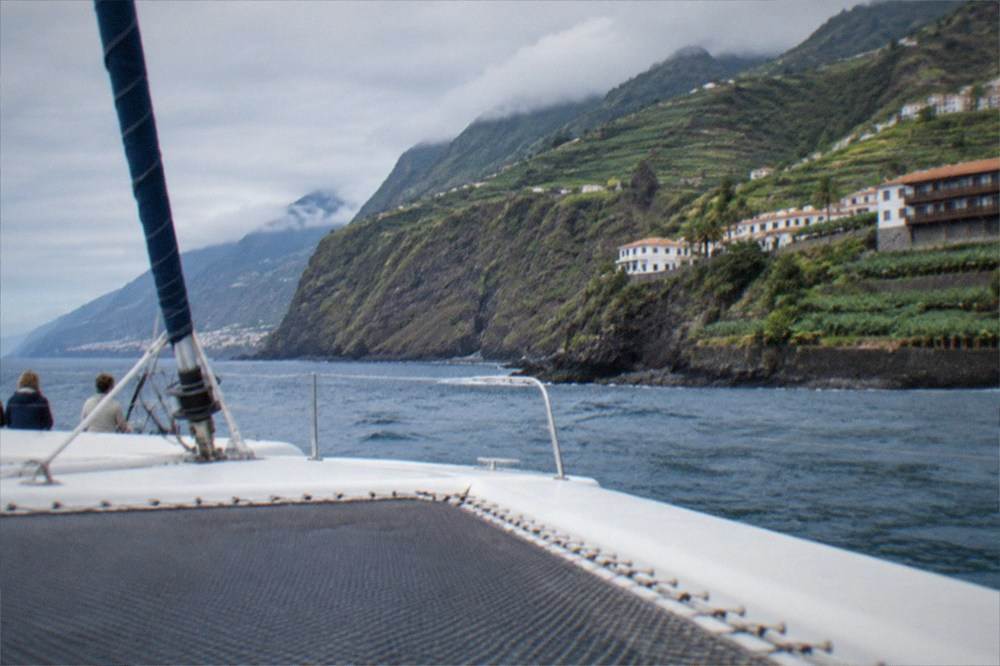 A catamaran at sea near tall cliffs with a coastal town below