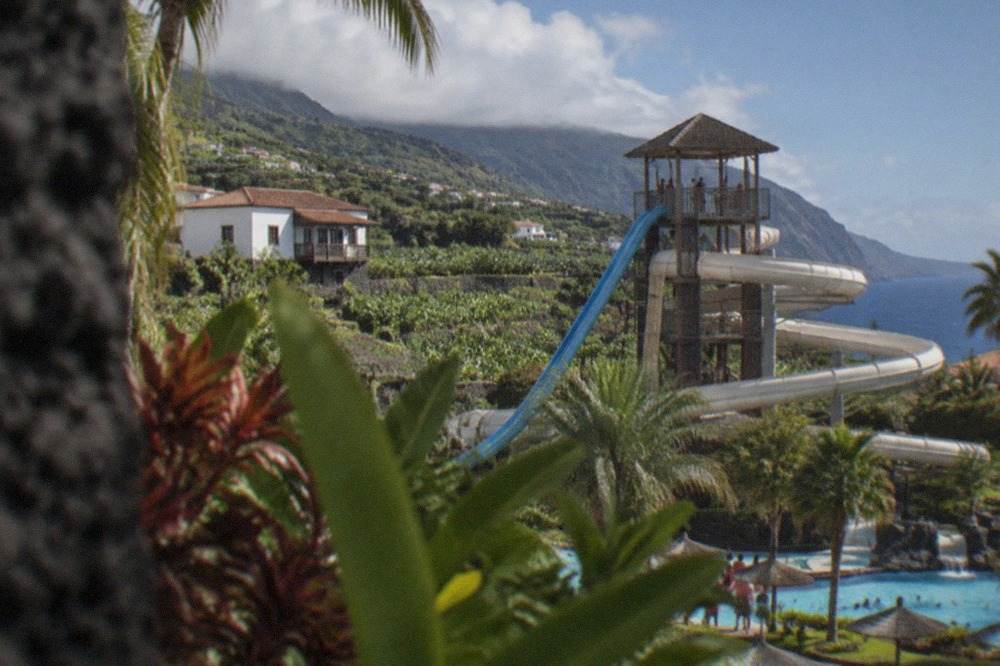 A water slide tower and tropical planting at a large Tenerife water park under a blue sky