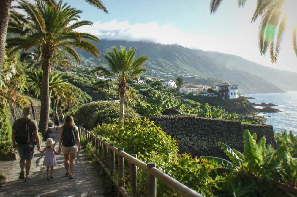 A family walking along a palm-lined path at a Tenerife theme park in bright sunshine