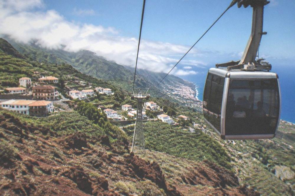 A cable car cabin ascending a volcanic mountainside above reddish rock formations