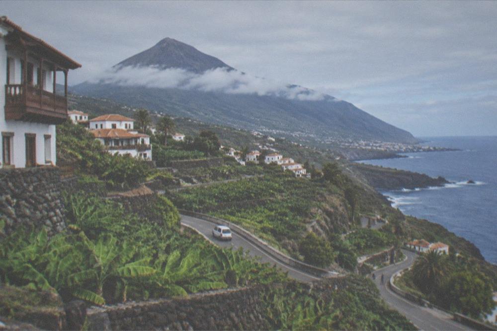 A wide volcanic landscape with a cone-shaped mountain and a road winding through red rock