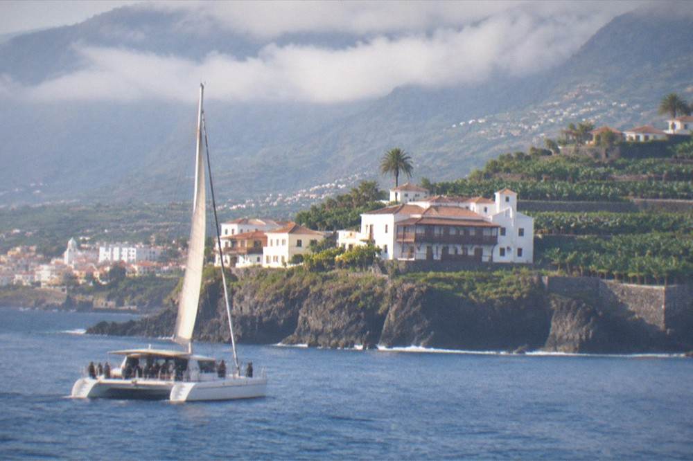 A catamaran with passengers sailing on calm blue water near a coastline