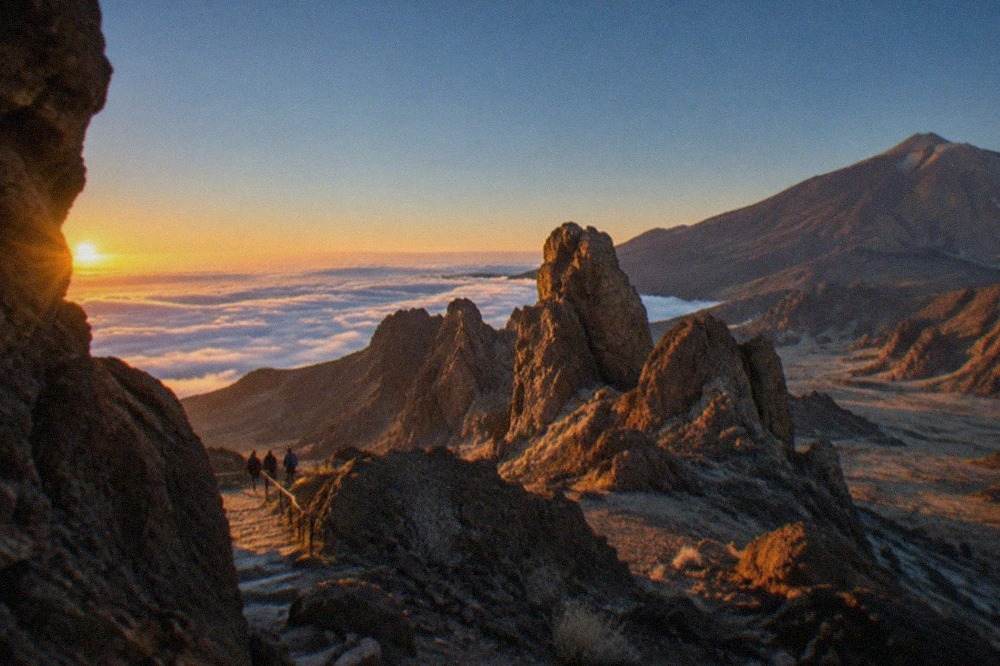 Rocky volcanic peaks rising above a sea of clouds at sunrise