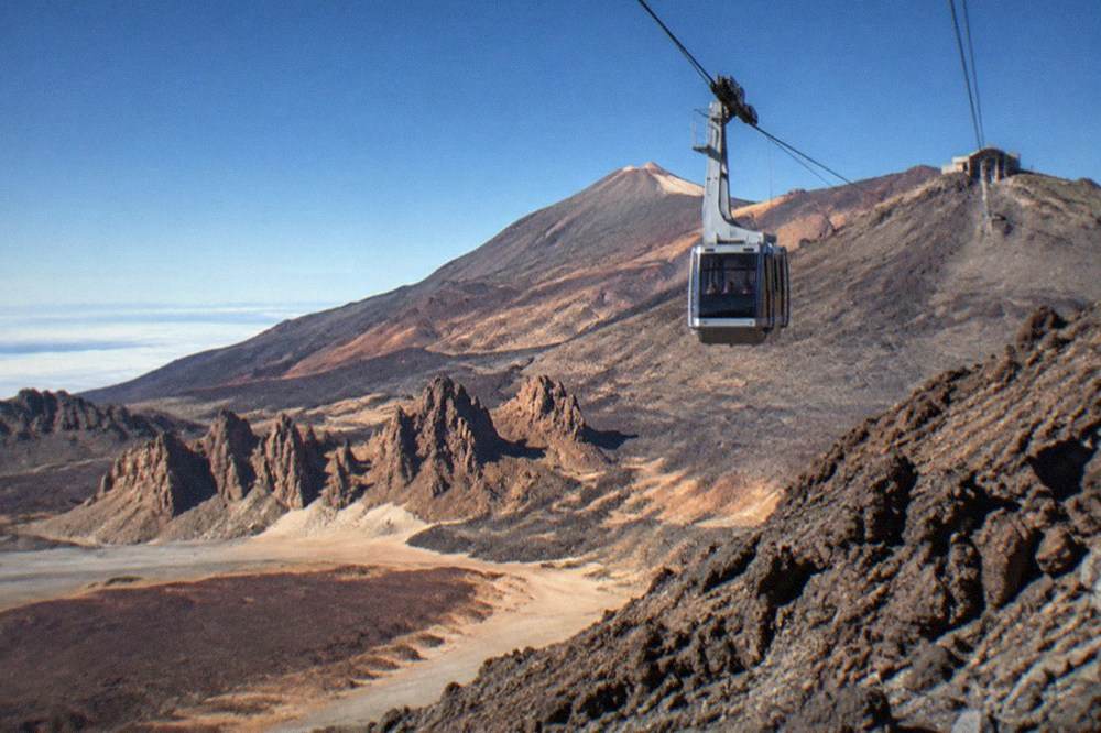 A cable car cabin travelling up a steep volcanic slope towards high station buildings