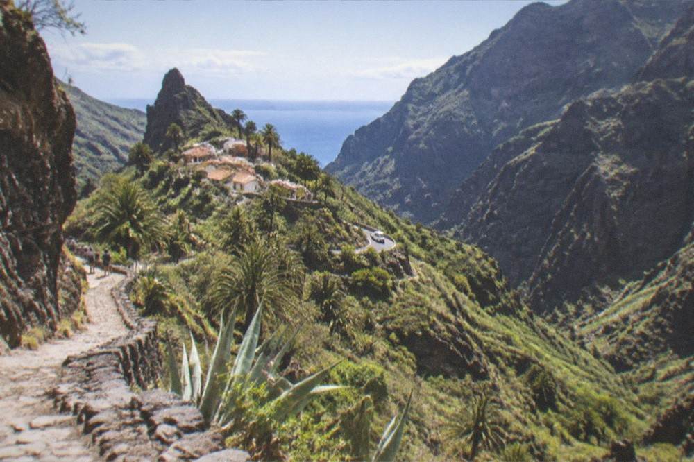 A narrow rocky gorge in the Masca ravine, steep green slopes and the sea a distant sliver far below