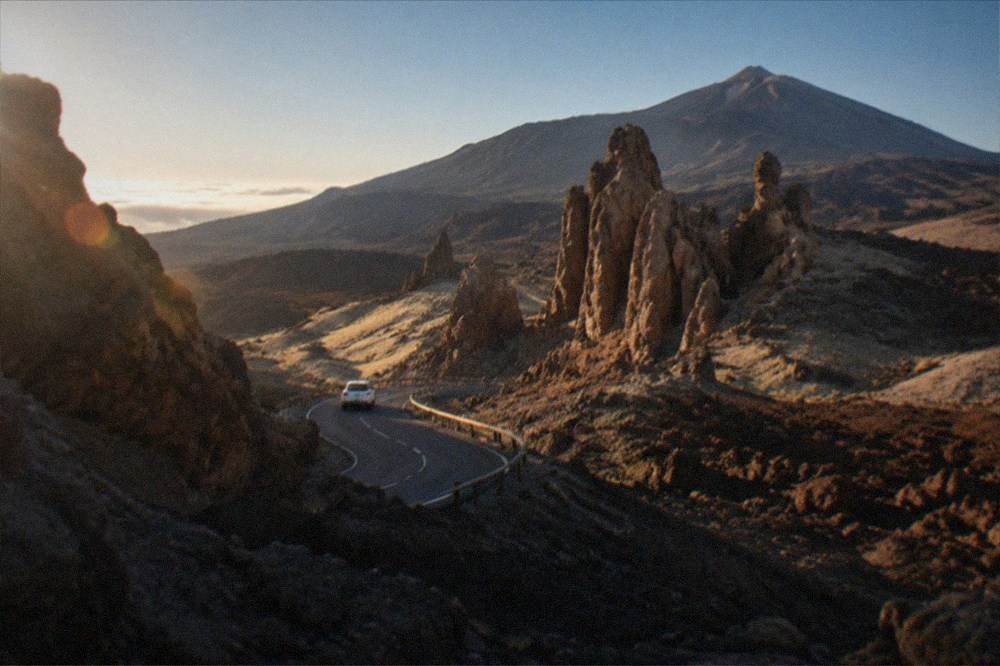 A road winding through mountainous terrain with a distant volcanic cone on the horizon