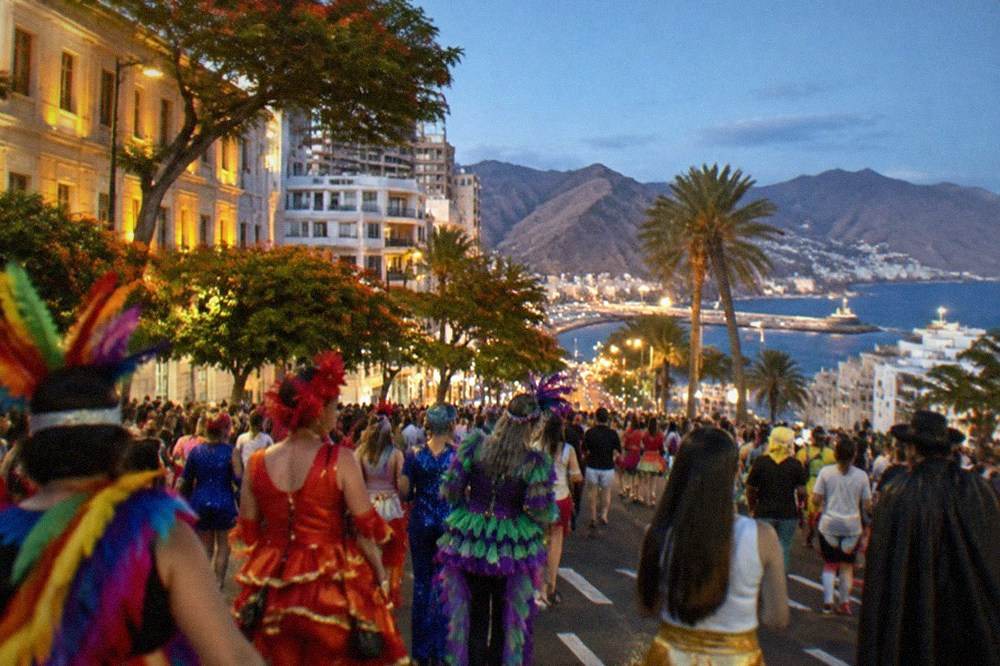 A busy evening street in Santa Cruz de Tenerife with crowds in colourful costumes between lit buildings