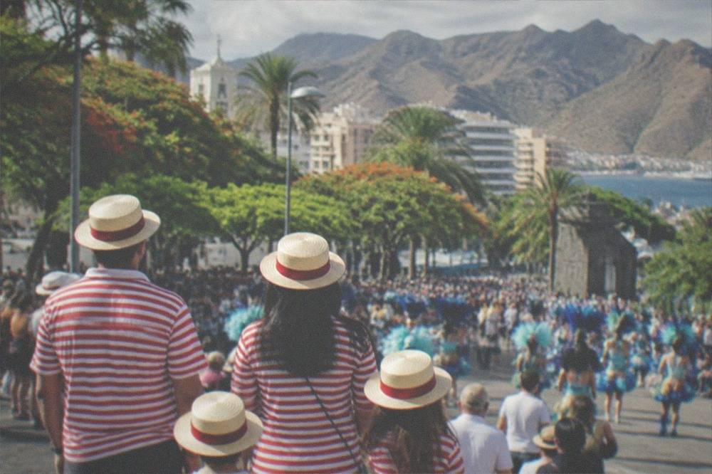 A family in matching costumes watching a daytime carnival street party in a sunny plaza