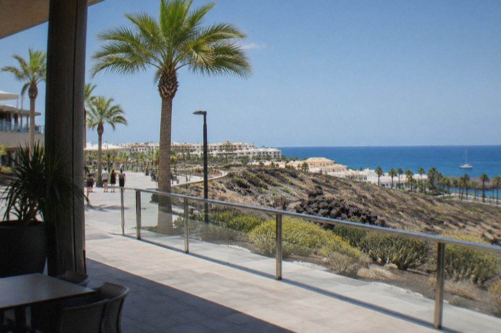 A modern shopping centre exterior with palm trees under a bright sky in Costa Adeje