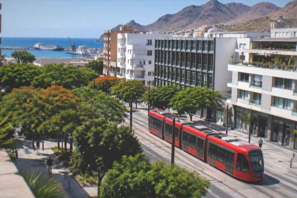 A red tram passing modern shopfronts on a city street in Santa Cruz