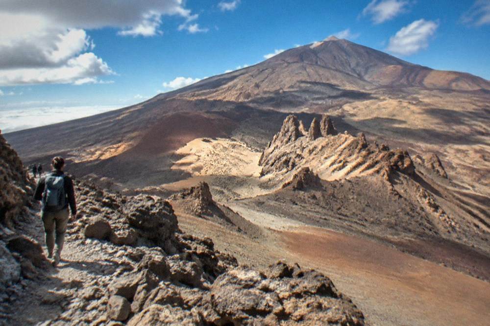A hiker with a backpack on a rocky volcanic trail high on Mount Teide