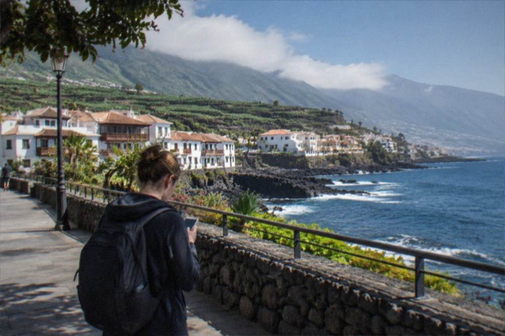 A traveller with a backpack looking at a phone on the seafront promenade at Puerto de la Cruz