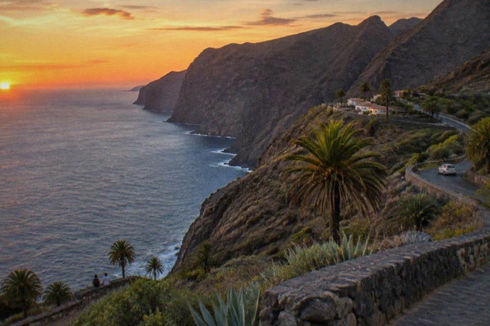 A clear coastal bay in Tenerife under a deep orange sunset sky