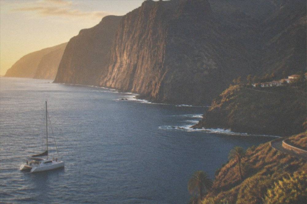 A catamaran on calm water near tall dark cliffs at golden hour