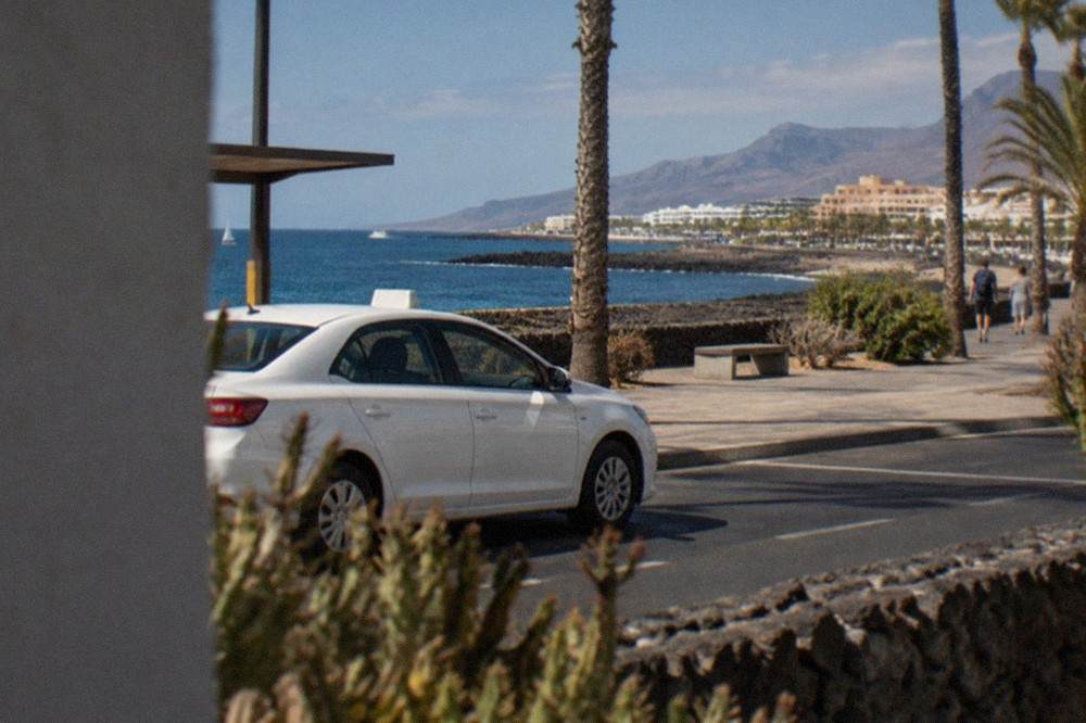 A white Tenerife taxi with its roof sign lit, waiting at a rank near the seafront