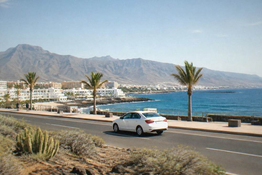 A taxi driving on a coastal road with mountains in the background in Tenerife