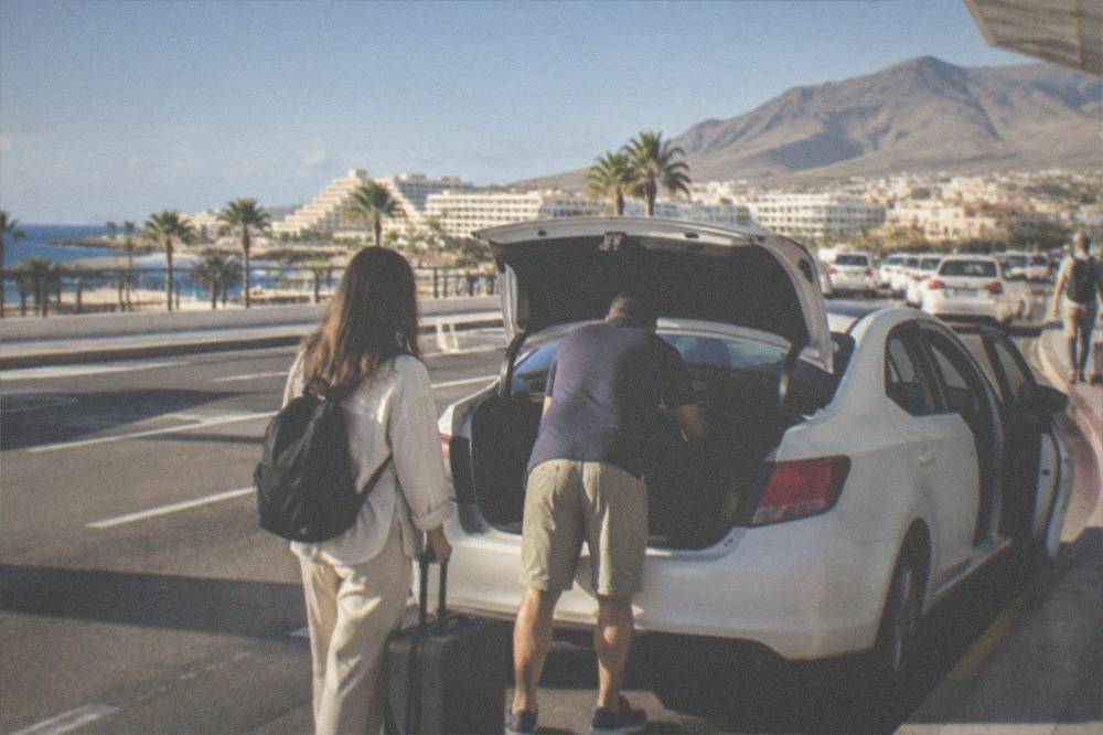 Passengers loading luggage into a white taxi outside an airport terminal in Tenerife