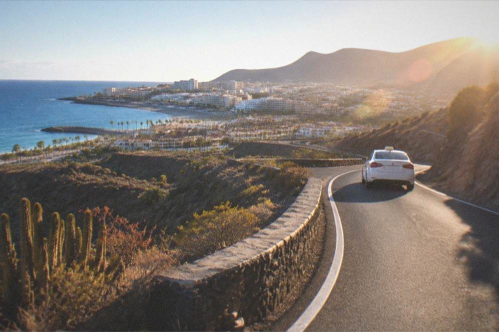 A taxi on a winding mountain road above green ravines in western Tenerife