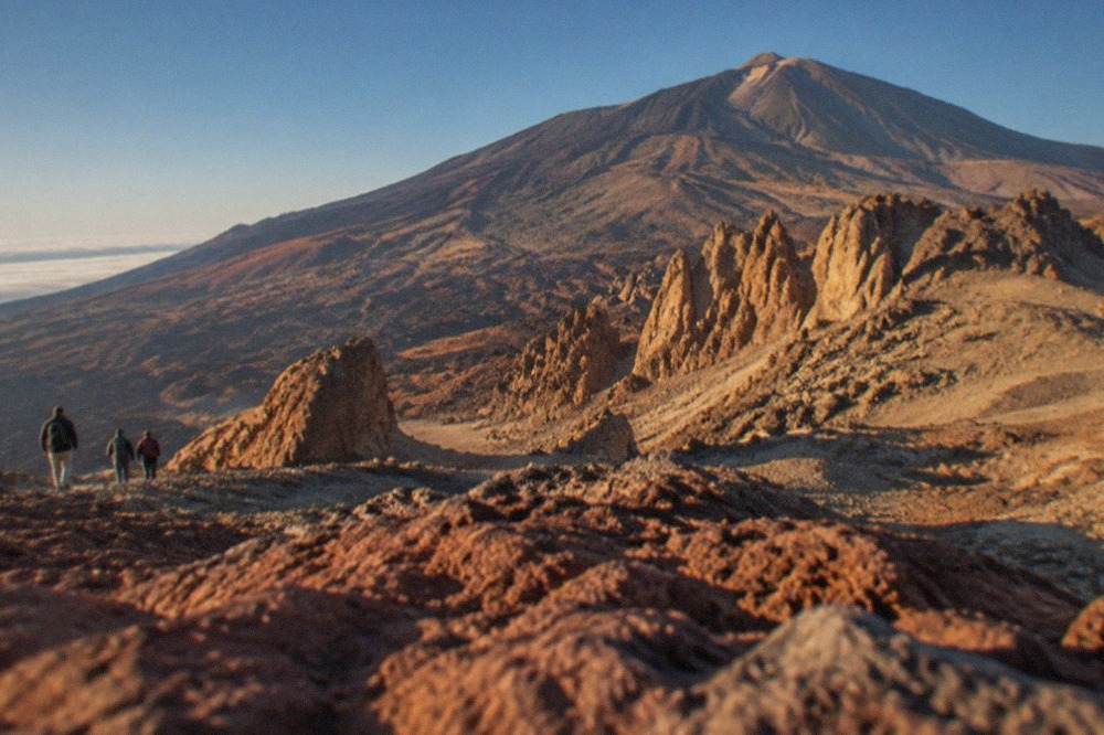 The rocky cone of Mount Teide rising above the red and grey volcanic landscape of the national park under a clear blue sky
