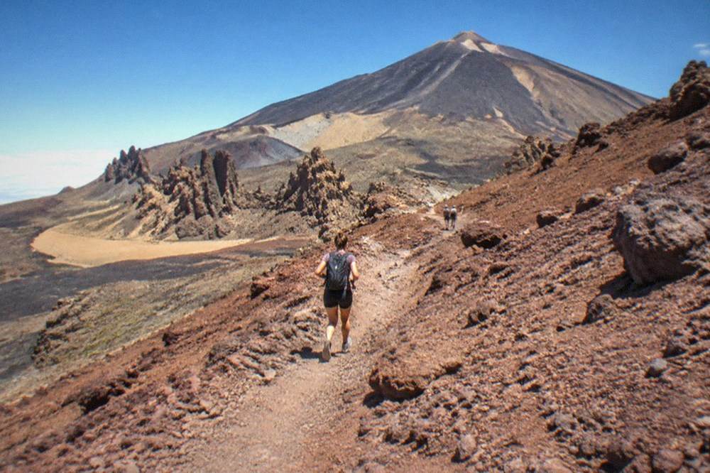 A rocky crater path with loose red volcanic stones winding uphill toward the summit cone