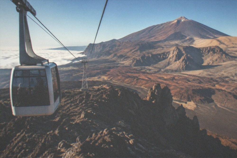 A cable car cabin travelling on its cable above dark volcanic rock formations