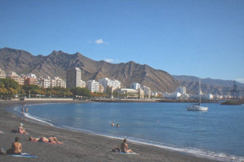 A sheltered sandy beach with calm water and sunbathers on a warm December day