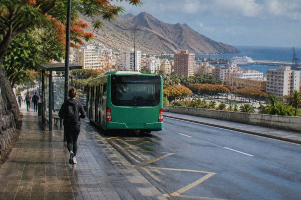 A green island bus at a stop on a Tenerife road with hills behind